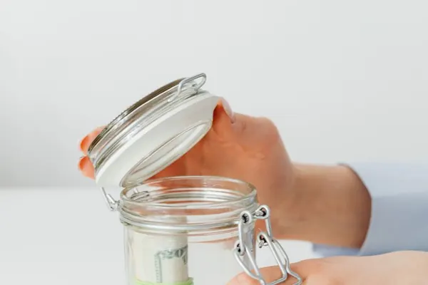 Unas manos abren un tarro de cristal con billetes dentro