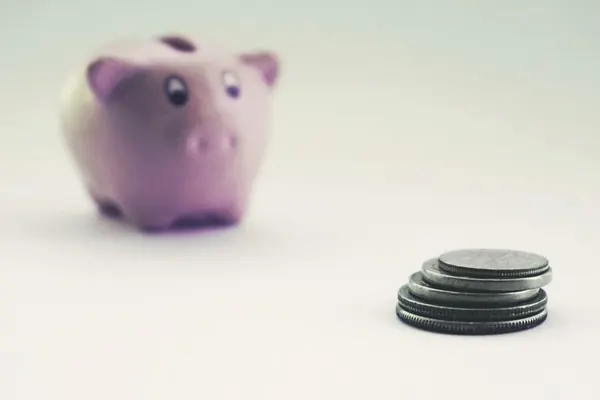 Una hucha rosa junto a una pila de monedas