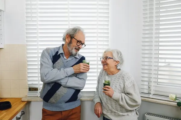 Una pareja de personas mayores brinda en la cocina de su casa