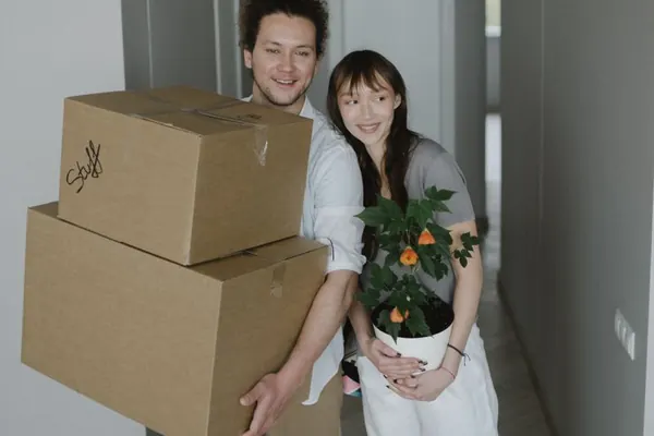 Una pareja con cajas de mudanza y una planta en el pasillo de su casa